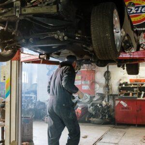 Mechanic repairing a vehicle in a busy workshop with various automotive tools.